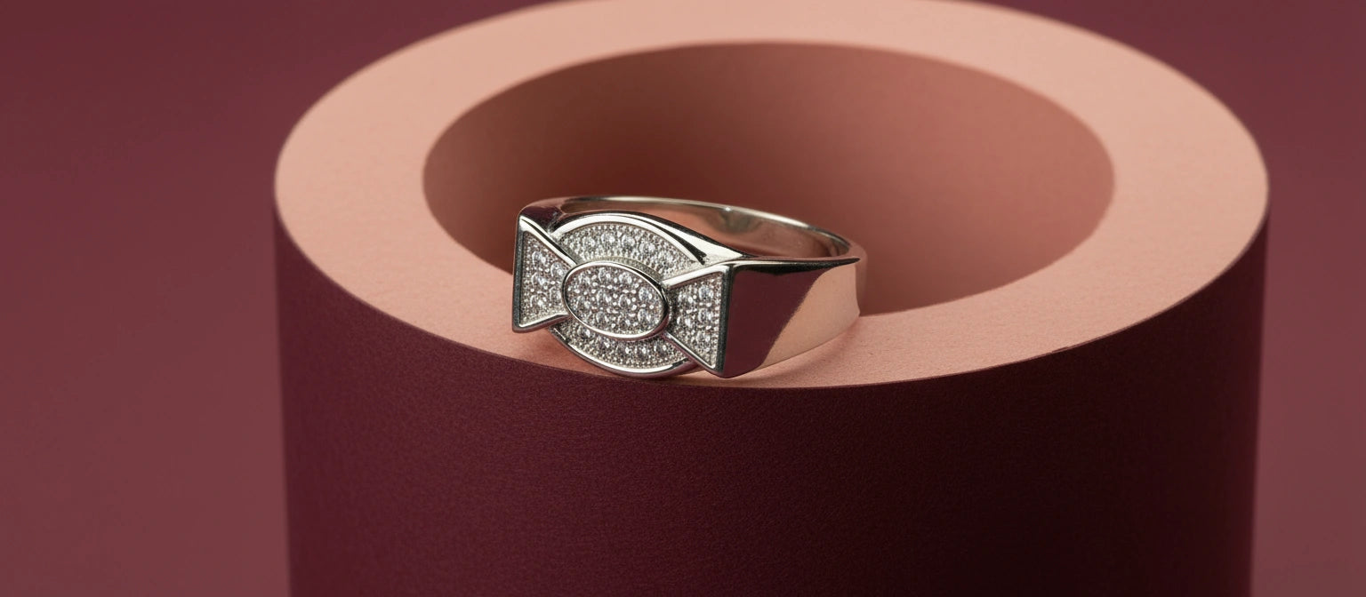 The Ambassador Pavé Ring by Narayan Jewellers, a 925 sterling silver ring with a full pavé oval and bowtie design, resting in a burgundy cylinder.