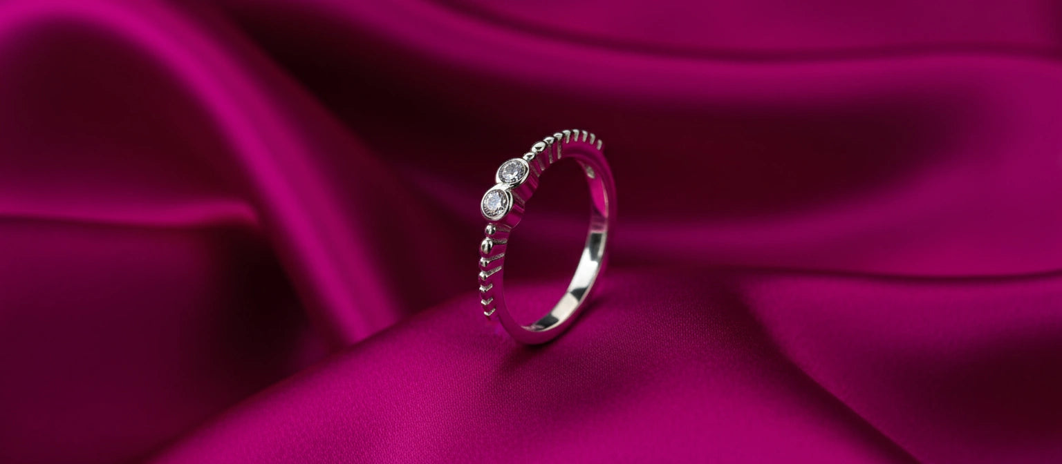 The Braveheart Duo Ring by Narayan Jewellers, a delicate 925 silver ring with two intertwined pavé hearts, on a crimson satin background.
