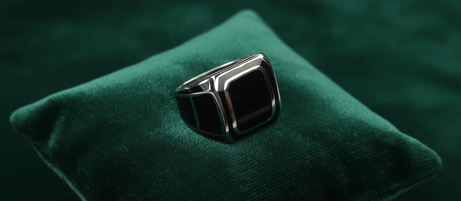 The Citadel Signet Ring by Narayan Jewellers, a square black enamel ring in 925 sterling silver, resting on a luxurious green velvet cushion.