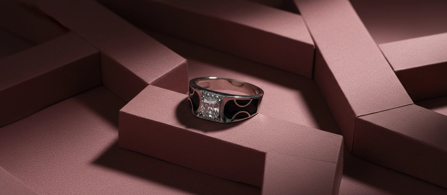 The Dynasty Curve Ring by Narayan Jewellers, a 925 silver ring with an emerald-cut stone and flowing black enamel details, on an architectural pink background.