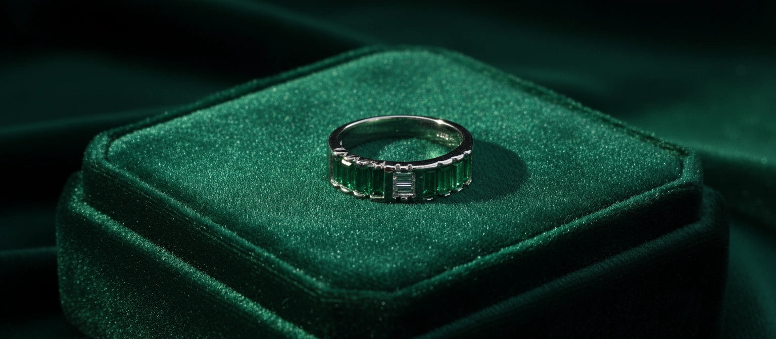 A 925 sterling silver eternity band featuring channel-set emerald green and clear baguette-cut cubic zirconia stones, displayed on a green velvet box.