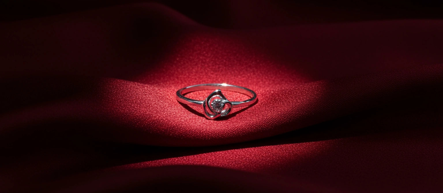 A delicate 925 sterling silver ring with a single round cubic zirconia solitaire held in a minimalist, petal-shaped swirl design, resting on red silk.