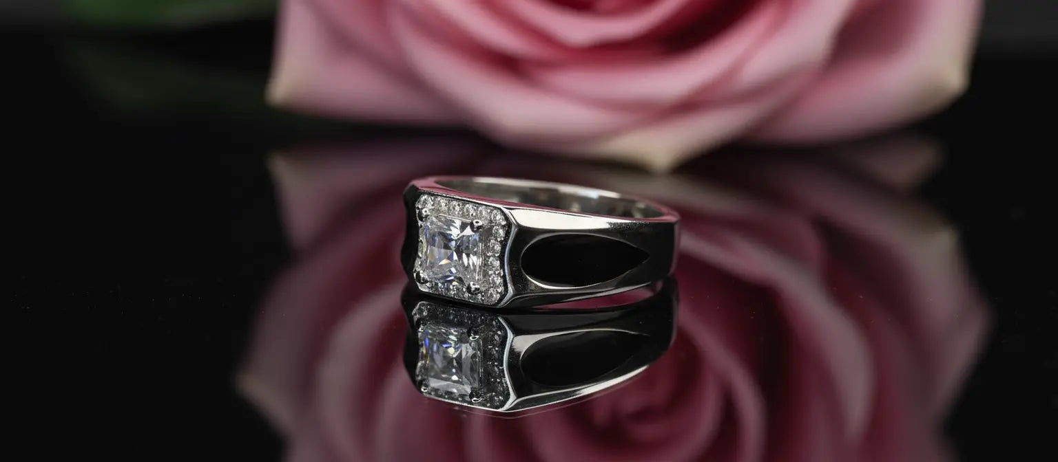 The Promise Solitaire Ring in 925 sterling silver, featuring a princess-cut halo stone, with its reflection on a black surface in front of a pink rose