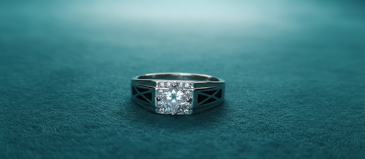 The Sovereign Cross Ring by Narayan Jewellers, a 925 sterling silver ring with a square halo stone and criss-cross black enamel band, on a textured teal surface.