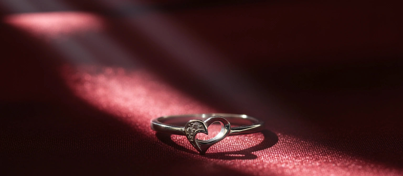 The Whisper Heart Ring by Narayan Jewellers, a delicate 925 silver open-heart ring, lying on a rich red satin cloth under a soft spotlight.